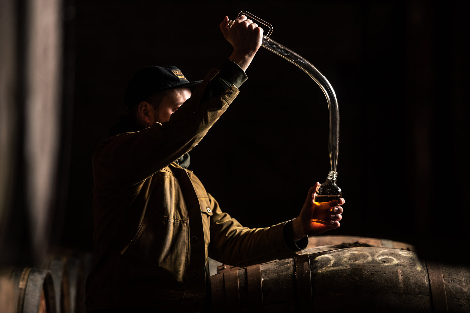 Man extracting whiskey from a barrel